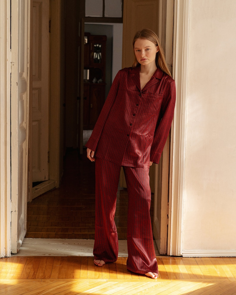 May include: A woman wearing a red and black checked pyjama set. The set includes a long-sleeved shirt and wide-leg trousers.