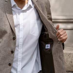 May include: A brown linen blazer with a white button-down shirt underneath. The blazer is unbuttoned and the inside lining is visible, showing a brown fabric with a white label that says "Oils".