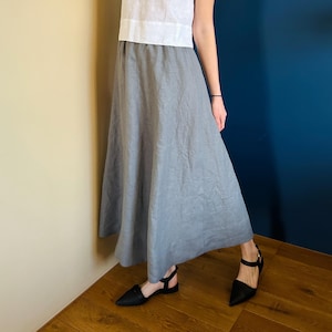 May include: A grey linen skirt with a flowing, A-line silhouette. The skirt is worn with a white top and black heeled sandals.