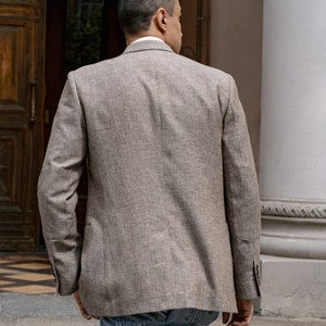 May include: A man wearing a brown linen blazer and blue jeans walks away from the camera.