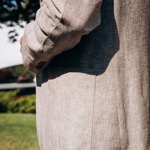 May include: A beige linen blazer with a patch pocket and a single button closure. The blazer is made of a textured fabric and has a relaxed fit.