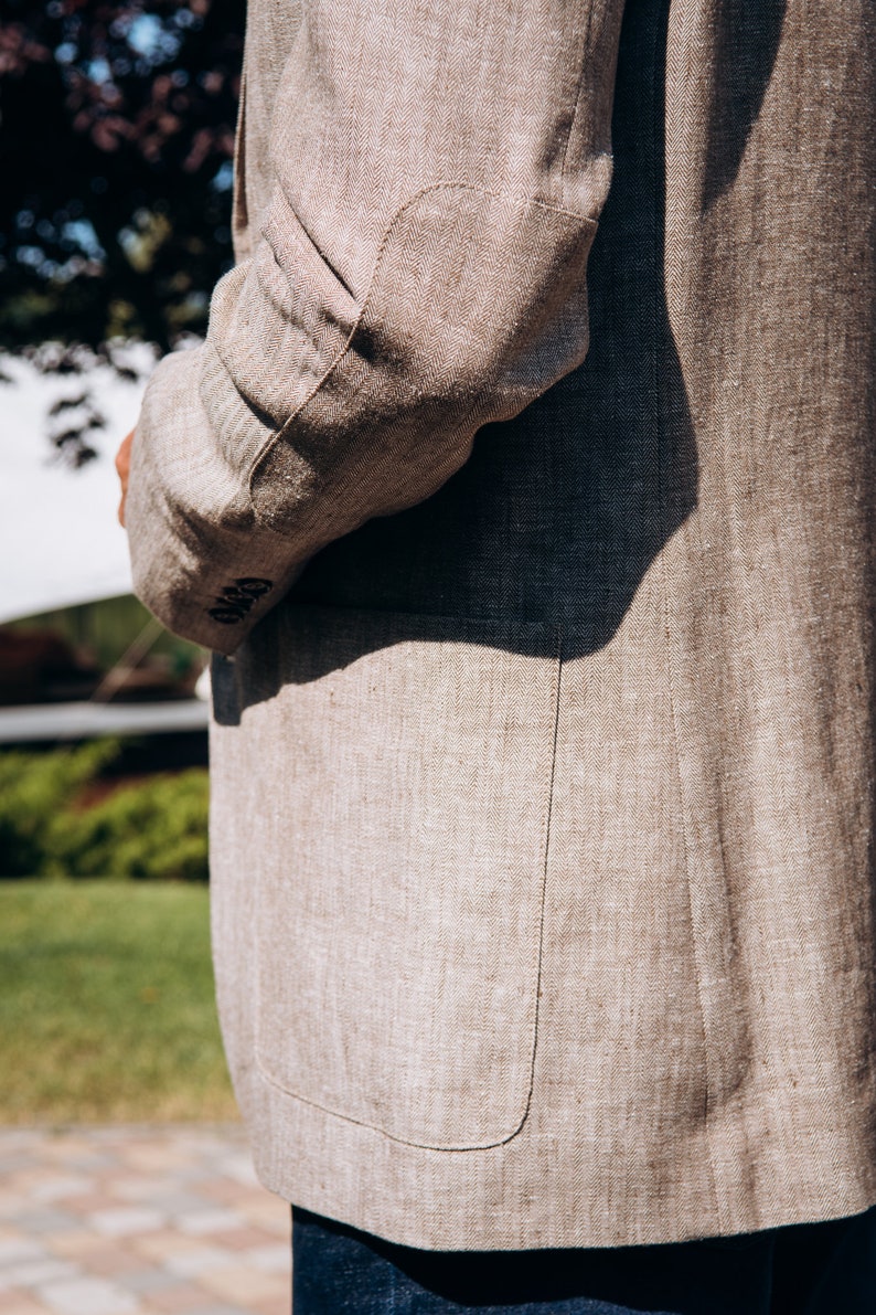 May include: A beige linen blazer with a patch pocket and a single button closure. The blazer is made of a textured fabric and has a relaxed fit.