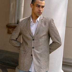 May include: A brown linen blazer with a white button-down shirt underneath. The blazer has two patch pockets and a button closure.
