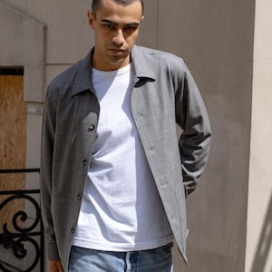 Puede incluir: Un hombre con una chaqueta gris sobre una camiseta blanca y pantalones vaqueros azules.