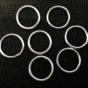 May include: Seven silver rings displayed on a black textured background. The rings are circular and have a smooth, reflective finish. The lighting accentuates the metallic quality of the rings. These rings could be used for jewellery making or other craft projects.