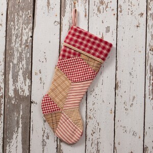 Puede incluir: Una media de Navidad de patchwork roja y marrón sobre un fondo blanco. La media está colgada en una pared de madera blanqueada.