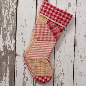May include: A red and tan patchwork Christmas stocking hangs on a whitewashed wooden wall.