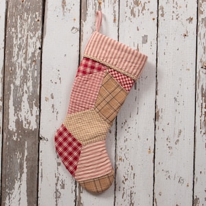 May include: A red and white patchwork Christmas stocking with a tan fabric background. The stocking is hanging on a white wooden wall.