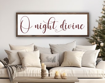 May include: A wooden sign with the text "O night divine" in a burgundy script font. The sign is hanging on a white wall above a white couch with pillows and a throw blanket.