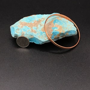 May include: A copper bangle bracelet resting on a piece of turquoise rock. A US coin is also in the image for size reference.