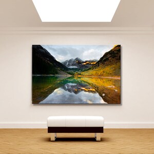 May include: A framed photograph of a mountain lake with a reflection of the mountains in the water. The mountains are covered in trees and snow. The sky is cloudy and the water is calm.