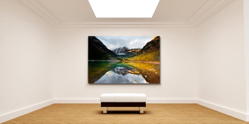 May include: A framed photograph of a mountain lake with a reflection of the mountains in the water. The mountains are covered in trees and snow. The sky is cloudy and the water is calm.