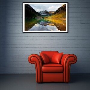May include: A red armchair with a single pillow sits in front of a brick wall with a framed photograph of a mountain lake reflecting the surrounding mountains.