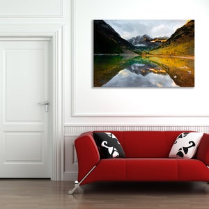 May include: A photograph of a mountain lake with fall foliage reflected in the water. The lake is surrounded by mountains with snow-capped peaks.