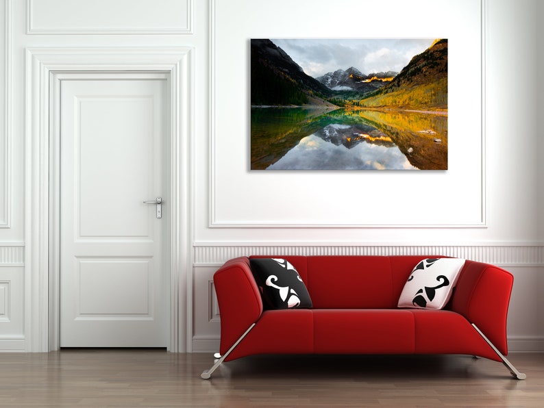 May include: A photograph of a mountain lake with fall foliage reflected in the water. The lake is surrounded by mountains with snow-capped peaks.