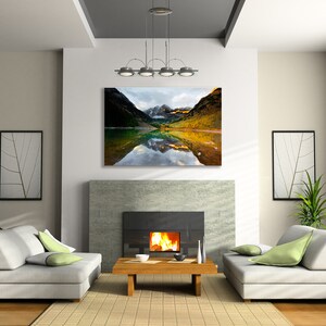 May include: A living room interior with a fireplace, two sofas, and a coffee table. A large framed photograph of a mountain lake with fall foliage and snow-capped peaks hangs above the fireplace.