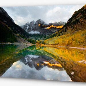 May include: A scenic landscape photograph of a mountain lake reflecting the surrounding fall foliage and snow-capped peaks. The water is a vibrant green and blue, reflecting the colors of the trees and mountains.