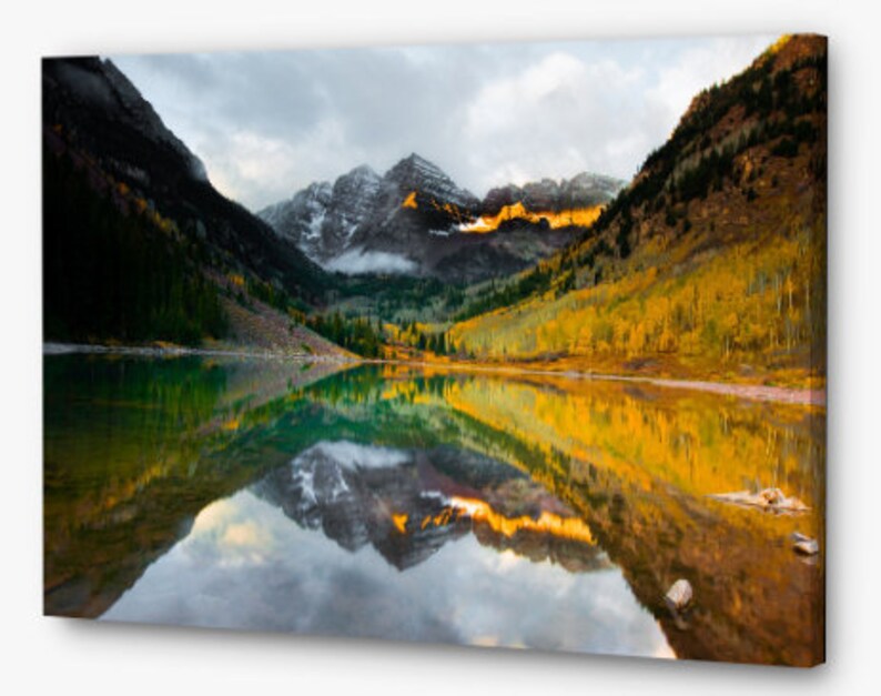 May include: A scenic landscape photograph of a mountain lake reflecting the surrounding fall foliage and snow-capped peaks. The water is a vibrant green and blue, reflecting the colors of the trees and mountains.