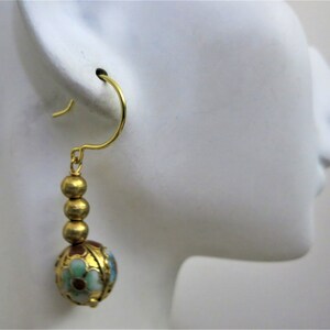 May include: Gold dangle earrings with a round, multi-colored enamel bead and three smaller gold beads. The enamel bead has a floral design with red, green, blue, and white enamel.