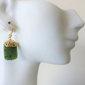 K&ouml;nnte beinhalten: Goldene Ohrringe mit einem gr&uuml;nen Jade-Stein Anh&auml;nger. Die Ohrringe haben ein filigranes Design.