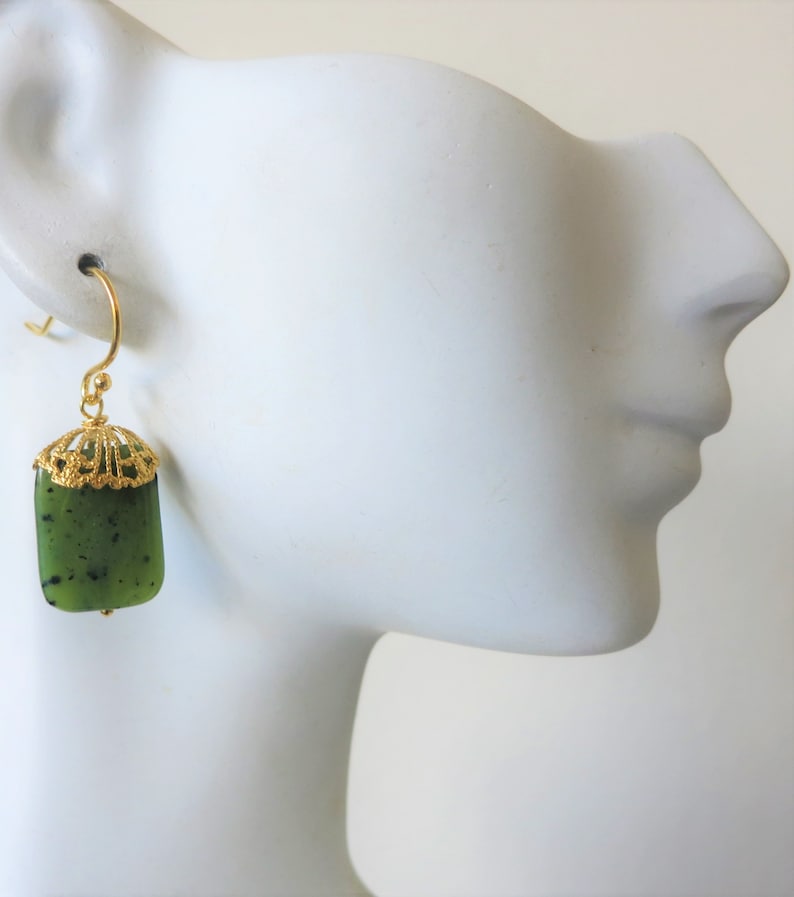 K&ouml;nnte beinhalten: Goldene Ohrringe mit einem gr&uuml;nen Jade-Stein Anh&auml;nger. Die Ohrringe haben ein filigranes Design.