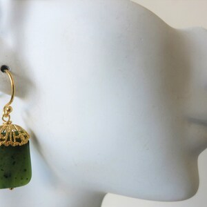 K&ouml;nnte beinhalten: Goldene Ohrringe mit einem Anh&auml;nger aus gr&uuml;nem Jade. Der Jadestein hat eine dunkelgr&uuml;ne Farbe mit schwarzen Flecken.