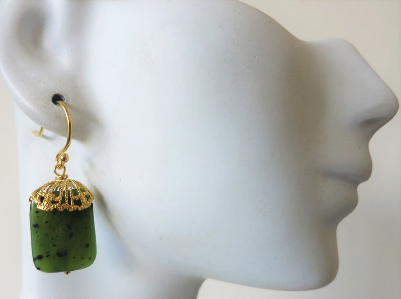 K&ouml;nnte beinhalten: Goldene Ohrringe mit einem Anh&auml;nger aus gr&uuml;nem Jade. Der Jadestein hat eine dunkelgr&uuml;ne Farbe mit schwarzen Flecken.
