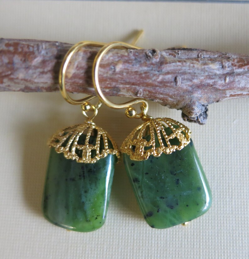 K&ouml;nnte beinhalten: Ein Paar gr&uuml;ne Jade-Ohrringe mit goldenen Filigran-Akzenten. Die Ohrringe sind rechteckig und haben ein zartes, filigranes Design.