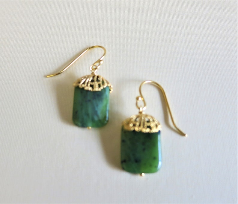 K&ouml;nnte beinhalten: Ein Paar goldene Ohrringe mit gr&uuml;nen Jade-Steinen. Die Ohrringe haben ein filigranes Design.