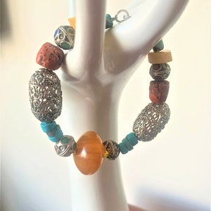 May include: A silver and turquoise beaded bracelet with a large amber bead in the center. The bracelet is made with a variety of beads, including silver filigree, turquoise, and red coral.