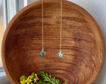 May include: A pair of gold-tone chain threader earrings, each featuring a small, round, moss-green and white speckled gemstone bead suspended from a delicate metal chain. The earrings are designed to be pulled through the earlobe for a hanging look.