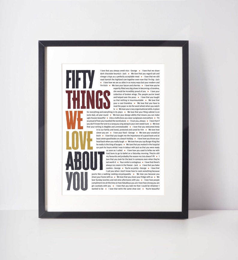 May include: A framed print with the words "FIFTY THINGS WE LOVE ABOUT YOU" in large, colorful text. The print is black and contains a list of loving sentiments in a smaller font. The overall theme is love and appreciation.
