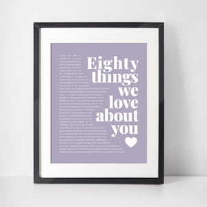 May include: Framed print with a lavender background and the text "Eighty things we love about you" in white. A white heart is at the bottom right. The print is in a black frame.