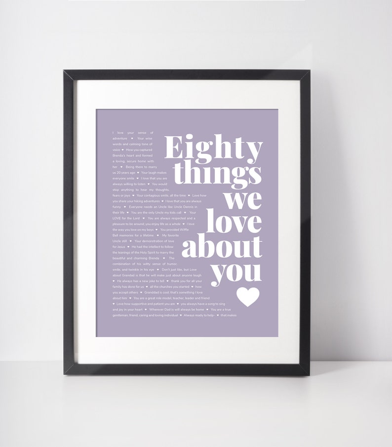 May include: Framed print with a lavender background and the text "Eighty things we love about you" in white. A white heart is at the bottom right. The print is in a black frame.