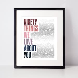 May include: Framed print with the words "NINETY THINGS WE LOVE ABOUT YOU" in a gradient of pink and blue. The print is in a black frame and contains a list of text in a smaller font.