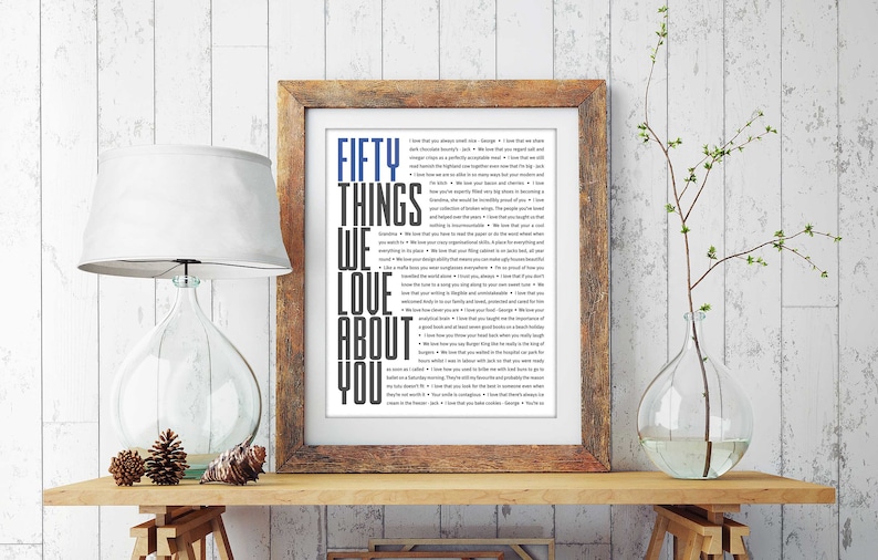 May include: A framed print with a white background and black text that reads "Fifty Things We Love About You". The frame is brown wood with a white mat.