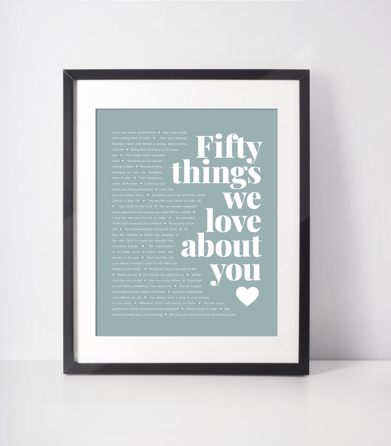May include: Framed print with a light blue background and white text. The text reads "Fifty things we love about you" with a heart symbol. The print is in a black frame.