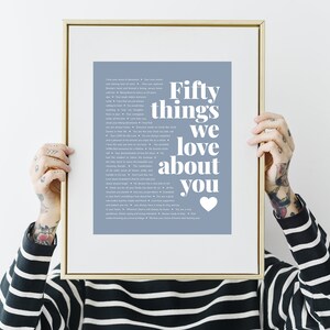 May include: A framed print with a light blue background and white text that reads "Fifty things we love about you" with a white heart at the bottom. The print is in a gold frame.