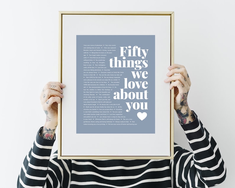May include: A framed print with a light blue background and white text that reads "Fifty things we love about you" with a white heart at the bottom. The print is in a gold frame.