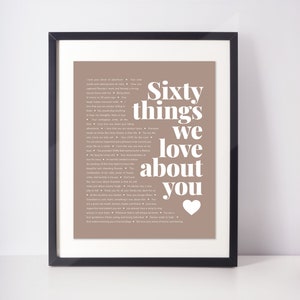 May include: Framed print with the text "Sixty things we love about you" in white on a taupe background. The print is in a black frame and includes a white heart graphic. The text lists various qualities and sentiments.