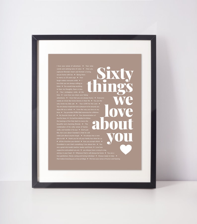 May include: Framed print with the text "Sixty things we love about you" in white on a taupe background. The print is in a black frame and includes a white heart graphic. The text lists various qualities and sentiments.