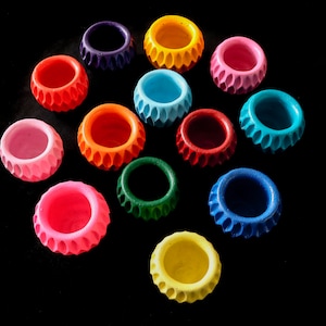 May include: A collection of 12 colourful, small, decorative bowls with a scalloped edge. The bowls are arranged in a circle on a black background.