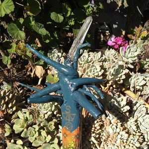 Op de afbeelding: Een wandelstok met een donkerblauwe geverfde basis en een kleurrijke, gepatroneerde schacht. De bovenkant van de stok is versierd met een helder kristal en draad.