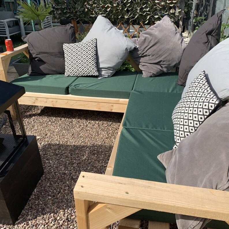 Op de afbeelding: Een houten buitenhoekbank met groene kussens en verschillende kussens met patronen. De bank is gemaakt van natuurlijk hout en heeft een rustieke uitstraling.
