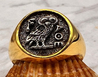 May include: A gold ring with a silver owl and the inscription "ΑΘΗΝΑΙΩΝ" on the face. The ring is sitting on a seashell.