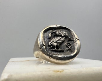 May include: A silver ring with an owl design. The owl is facing right and has large, round eyes. The ring is set on a white surface.