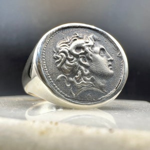 May include: Silver ring featuring a detailed design of a person's head in profile.