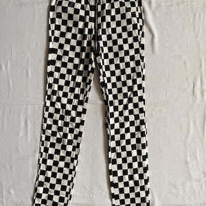May include: Black and white checkered pants with a front zipper. The pants have a high waist and a slim fit. The checkered pattern is made up of black and white squares.