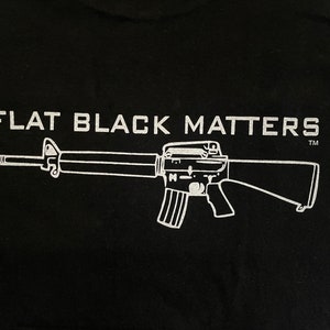 May include: Black t-shirt with a white graphic of a rifle and the text "FLAT BLACK MATTERS" with a trademark symbol.