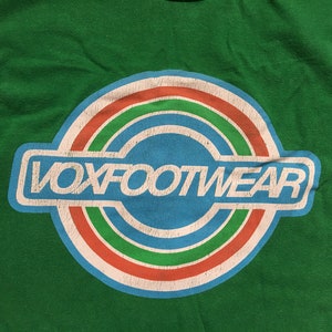 May include: A green t-shirt with a white circle logo that says "VOXFOOTWEAR" in white letters. The circle has three concentric rings in red, green, and blue.